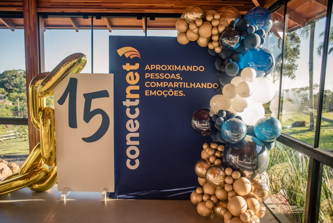Painel de 15 anos da Conectnet com arco de balões dourados e azuis